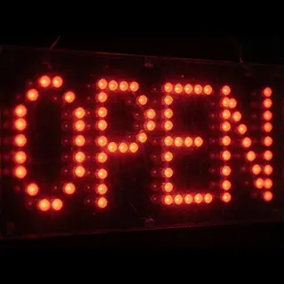 The word 'OPEN' displayed on a red LED sign with glowing pix