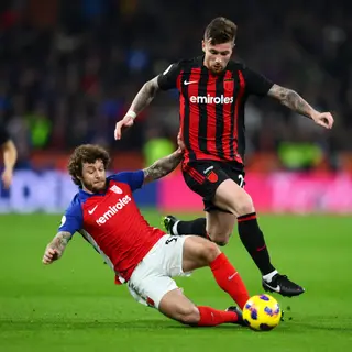 Two soccer players mid-tackle, one sliding and the other jum