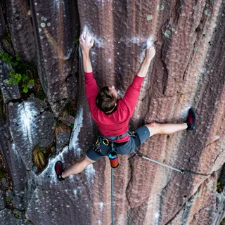 A rock climber clinging to a cliff face with arms and legs e