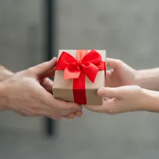 One person handing a small gift box to another person, both 