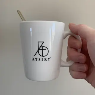 A person holding a white ceramic coffee mug by the handle wi