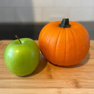 A green apple and an orange pumpkin on a wooden cutting boar