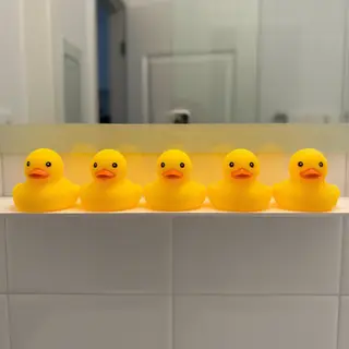 Exactly 5 yellow rubber ducks sitting in a row on a bathroom