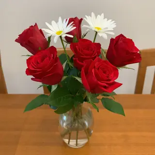 4 red roses and 2 white daisies in a glass vase on a table