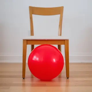 A red ball underneath a wooden chair