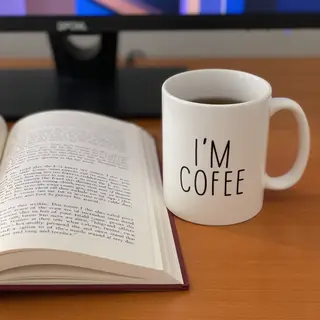 A coffee mug next to an open book on a desk