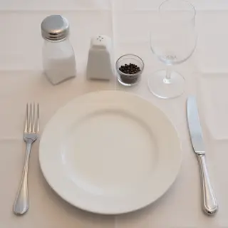 A dinner table scene with a plate, fork, knife, wine glass, 