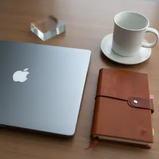 A workspace desk with a brushed aluminum laptop, a leather-b