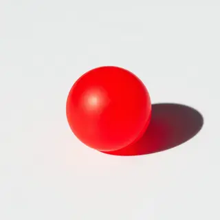 A red sphere on a white surface with a single shadow cast to