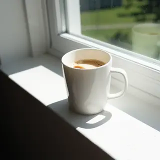 A coffee mug on a sunny windowsill casting a sharp shadow to