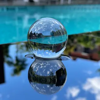 A clear glass sphere sitting on a mirror surface near a pool