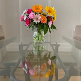 A vase of flowers on a glass table with a clear reflection v