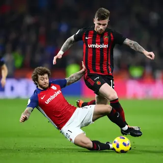 Two soccer players mid-tackle, one sliding and the other jum