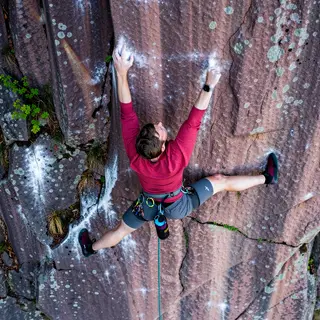 A rock climber clinging to a cliff face with arms and legs e