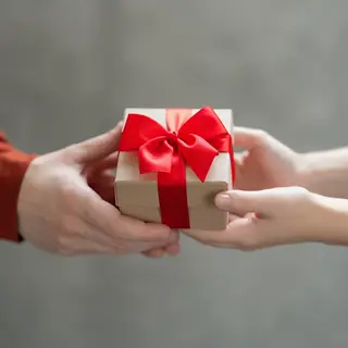 One person handing a small gift box to another person, both 