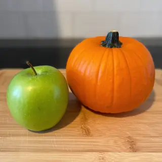 A green apple and an orange pumpkin on a wooden cutting boar
