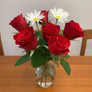 4 red roses and 2 white daisies in a glass vase on a table
