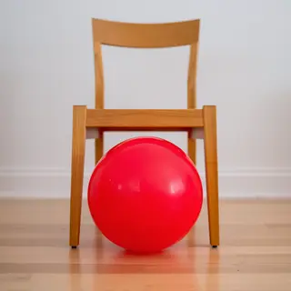 A red ball underneath a wooden chair