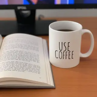A coffee mug next to an open book on a desk