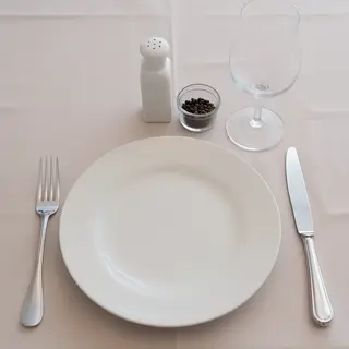 A dinner table scene with a plate, fork, knife, wine glass, 