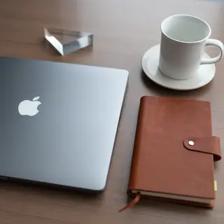 A workspace desk with a brushed aluminum laptop, a leather-b