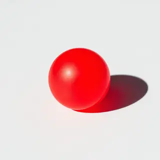 A red sphere on a white surface with a single shadow cast to