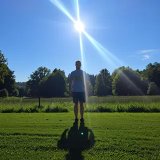 A person standing outdoors at midday with a short shadow dir