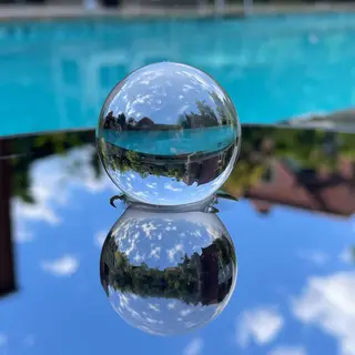 A clear glass sphere sitting on a mirror surface near a pool