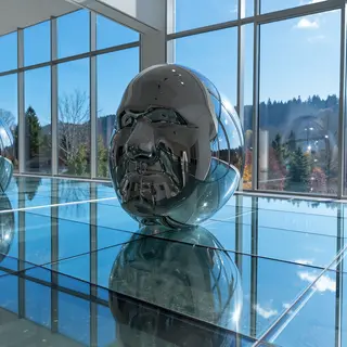A chrome sculpture in a room with a glass floor and large wi