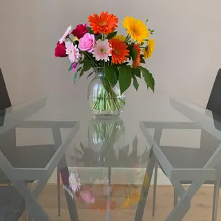 A vase of flowers on a glass table with a clear reflection v