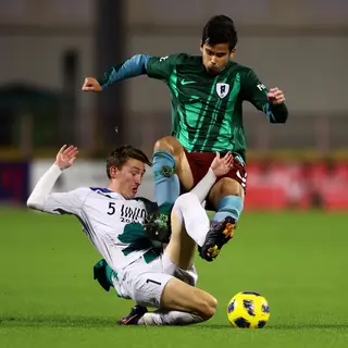 Two soccer players mid-tackle, one sliding and the other jum