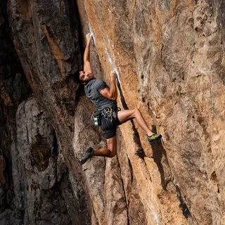 A rock climber clinging to a cliff face with arms and legs e