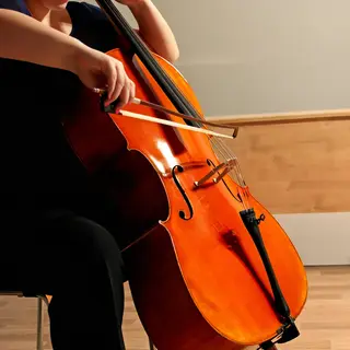 A cellist seated with correct posture, legs around the instr