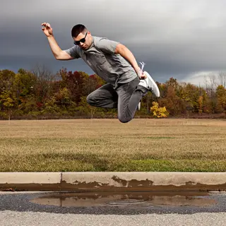 A man captured mid-jump over a puddle, body in the air with 