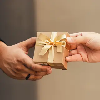 One person handing a small gift box to another person, both 