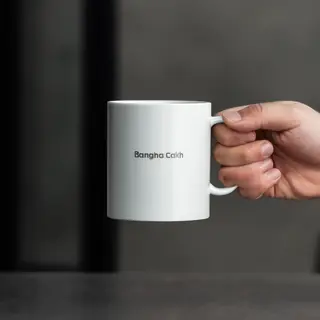 A person holding a white ceramic coffee mug by the handle wi
