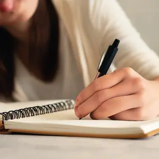 A woman writing in a notebook with a pen gripped correctly i