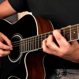 A person playing an acoustic guitar with left hand on the fr
