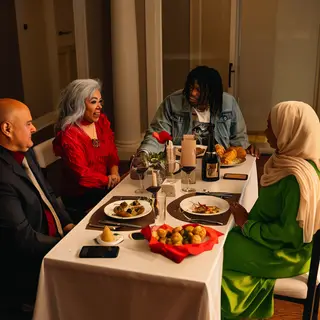 Four people at a dinner table: a bald man in a suit, a woman