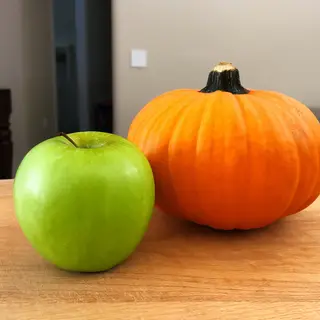 A green apple and an orange pumpkin on a wooden cutting boar