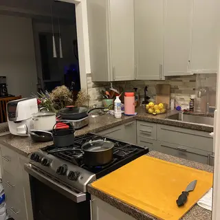 A kitchen with pots, pans, a stove, and a cutting board but 