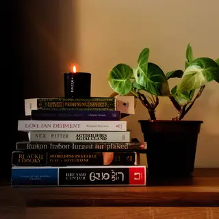 A candle on top of a stack of books, the books next to a pot