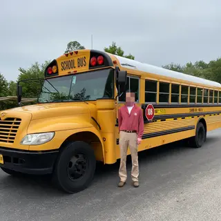 A person standing next to a yellow school bus, showing reali