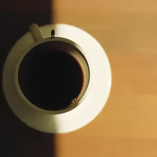 A tiny person standing on the rim of a coffee cup, looking d