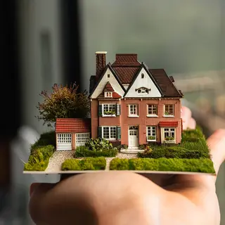 A miniature house sitting on the palm of someone's hand