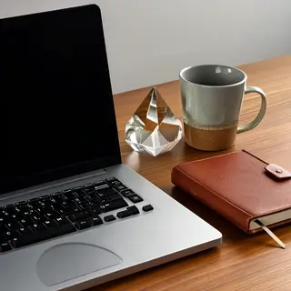 A workspace desk with a brushed aluminum laptop, a leather-b