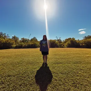 A person standing outdoors at midday with a short shadow dir