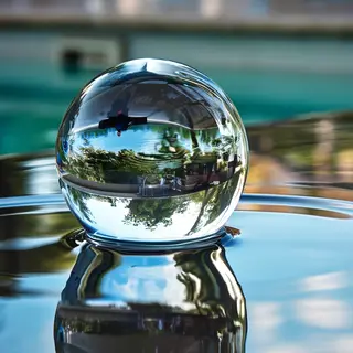 A clear glass sphere sitting on a mirror surface near a pool