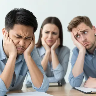 Three coworkers in a meeting: one looking frustrated with fu