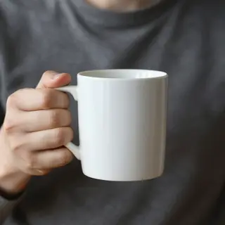 A person holding a white ceramic coffee mug by the handle wi